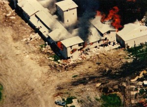 The Branch Davidian property after it was set on fire by tanks. Attribution: wiki user Carolmooredc